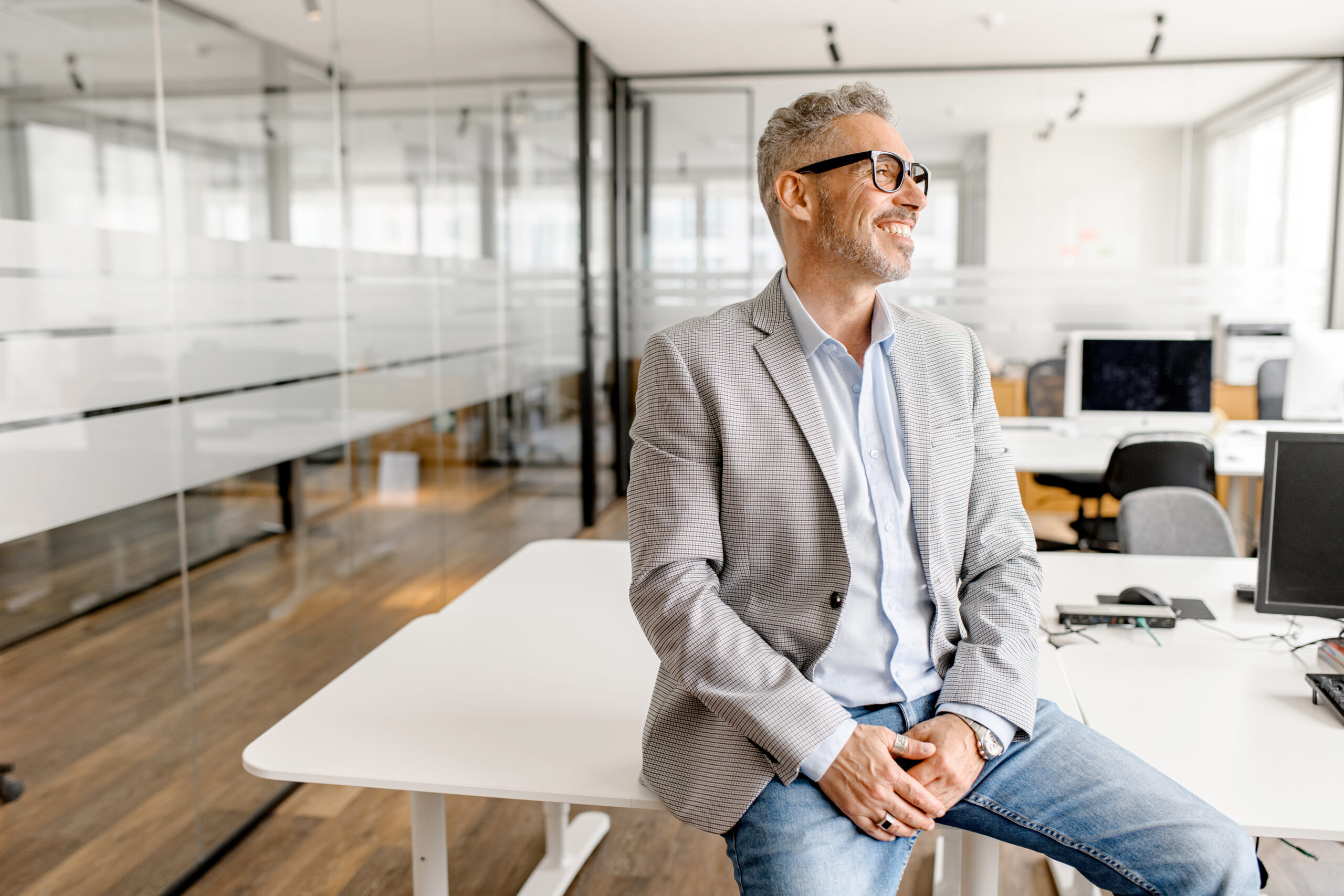 Serene modern middle aged businessman in formal wear leaned on the desk looking away, inspired and calm mature business owner at the office, confident grey-haired man in relaxed pose Serene Modern Middle Aged Businessman In Formal Wear Leaned On The Desk Looking Away