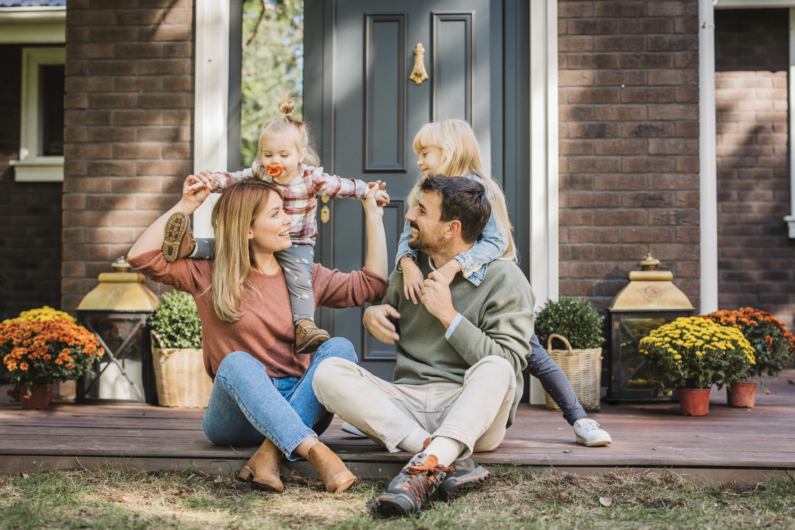 Young family with two kids having fun in front of there house. Porch is decorated with flowers. Young Family Enjoying In Sunny Day